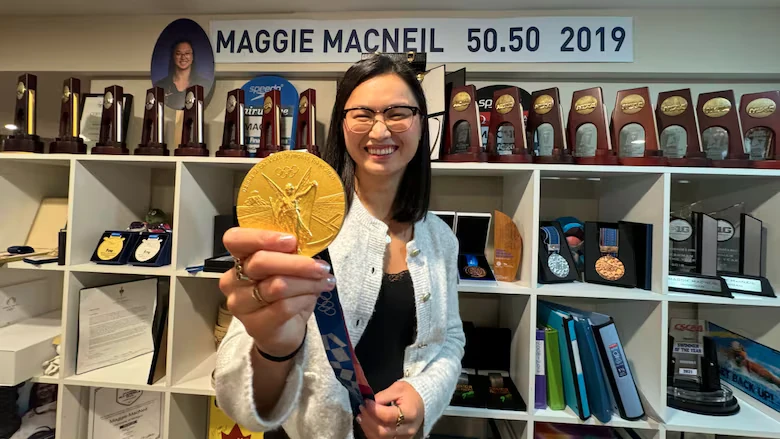 Retired Maggie Mac Neil poses at home in London, Ont., with her 100-metre butterfly gold medal from the Tokyo Olympics. (Devin Heroux/CBC Sports)