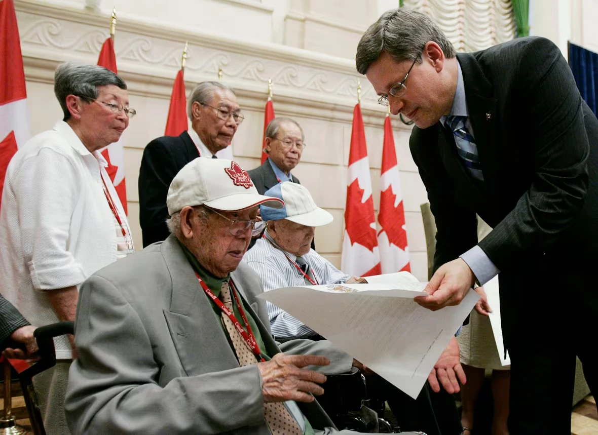 Former Prime Minister Stephen Harper presents a copy of the Canadian government's official apology to survivors of the Chinese Head Tax. (Photo: Tom Hanson / Canadian Press, via CBC)